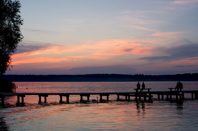 Silhouette people on pier over lake against sky during sunset