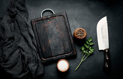 Empty wooden cutting board, salt, pepper and knife on black wooden table, top view