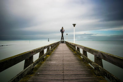 Empty jetty leading to sea against cloudy sky