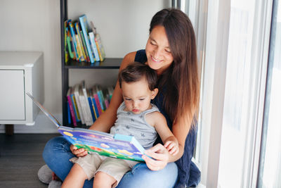 Mother and daughter sitting on book at home