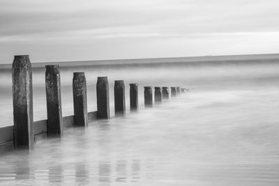 Wooden posts in sea against sky