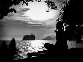 Silhouette woman sitting by sea against sky