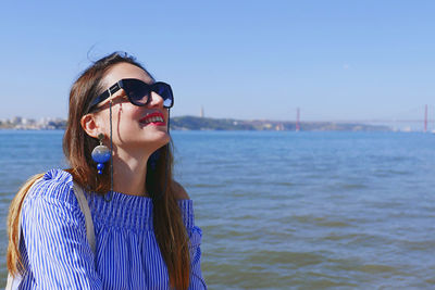 Portrait of young woman wearing sunglasses standing by sea against sky