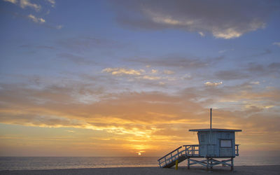 Lifeguard hut on beach against dramatic sky during sunset