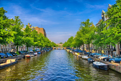 Sailboats moored in canal amidst city against sky