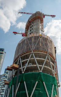 Low angle view of crane by building against sky