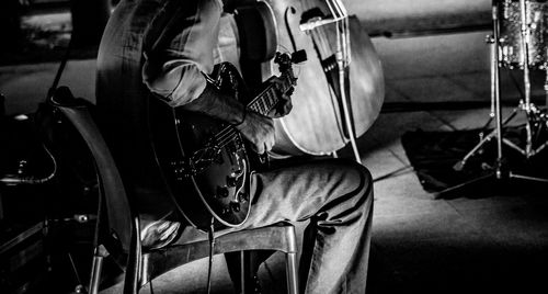 Midsection of man playing guitar while sitting on chair at night