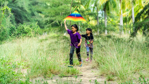Blurred motion of girls flying kite while walking on field against trees in park