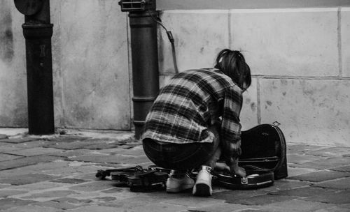 Rear view of woman with musical instrument crouching on footpath