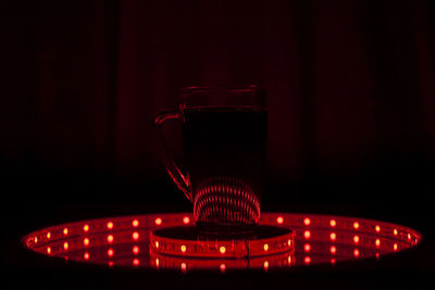 Close-up of drink in mug on illuminated lighting equipment in dark room