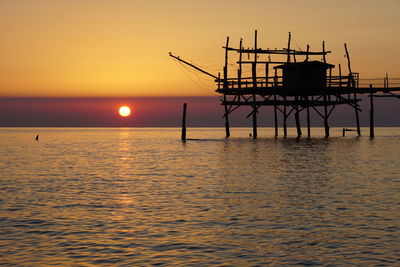 Silhouette built structure over sea against sky during sunset