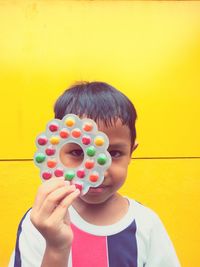 Portrait of boy holding toy against yellow wall