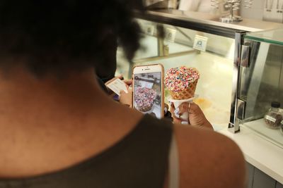 Rear view of woman holding mobile phone and taking a photo of her ice cream 