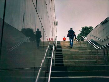 Rear view of man walking on staircase against sky