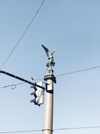 Low angle view of bird perching on cable against clear sky