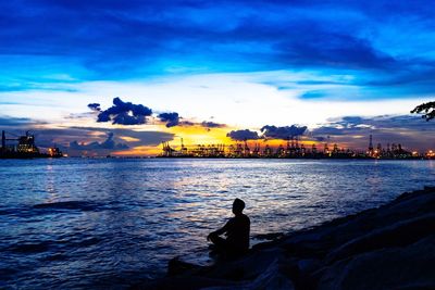 Silhouette man sitting by sea against sky during sunset