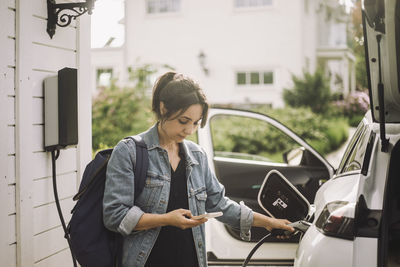 Woman charging electric car while using smart phone