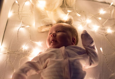 High angle view of baby girl lying on illuminated bed at home