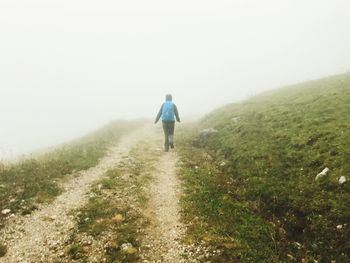 Rear view of man walking on mountain against sky