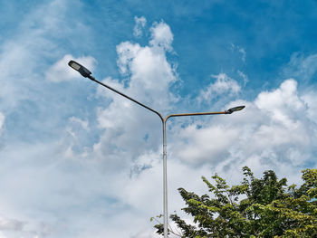 Low angle view of street lamps post against blue cloudy sky