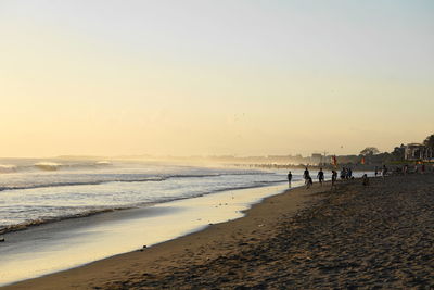 People on beach against clear sky during sunset