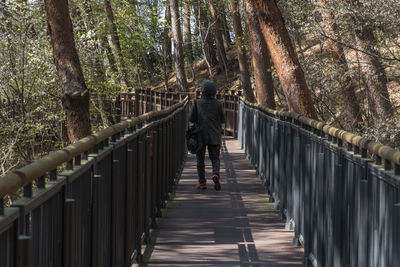 Rear view of woman walking on footbridge in forest