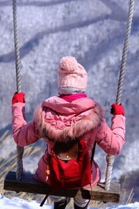 Low angle view of young woman standing on the swing against sky during winter