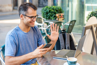 Young latin man video calling with computer outside.