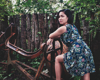 Portrait of young woman standing by rusty old machine in forest