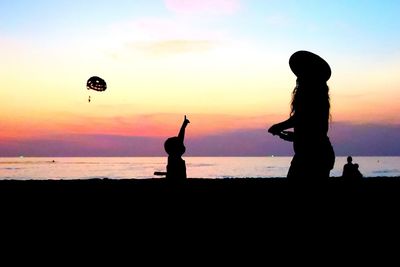 Silhouette people on beach against sky during sunset