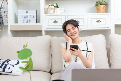 Young woman using phone while sitting on sofa at home