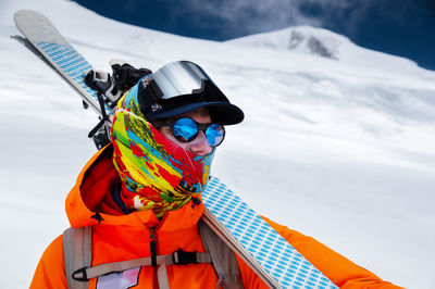 Mountain portrait of a professional freeride skier in orange clothing with ski poles and skis 