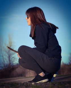 Side view of woman crouching on field against clear sky