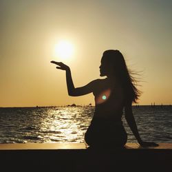 Woman standing by sea against sky during sunset