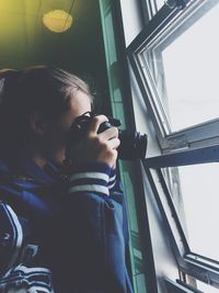 Side view of woman photographing through window