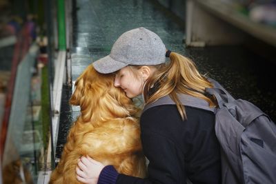 Side view of smiling teenage girl kissing dog at home