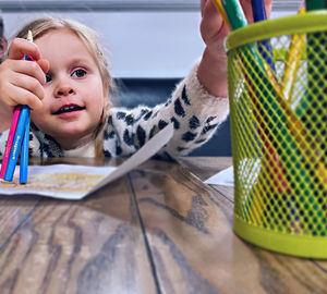 Cute girl holding colored pencils on table