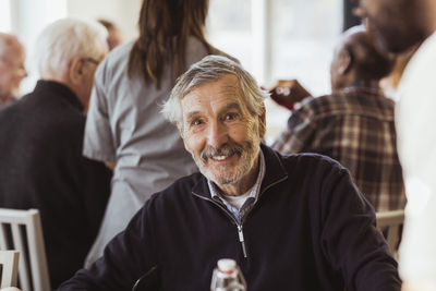 Portrait of smiling senior man with caregiver and friends in background at nursing home