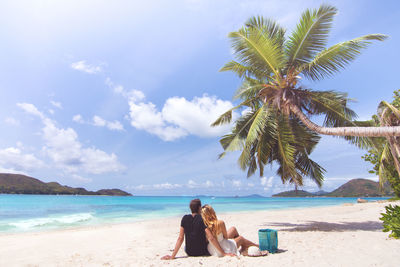 Rear view of couple sitting on beach against sky