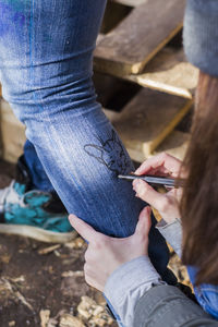 Cropped hand of woman drawing on friend leg