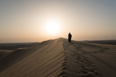 Man standing on sand dune in desert against sky during sunset
