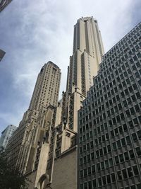 Low angle view of skyscrapers against cloudy sky