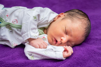 Newborn baby isolated sleeping in white cloth with purple background from different angle