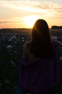 Rear view of woman standing on field against sky during sunset