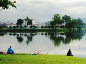 People relaxing on lakeshore against cloudy sky