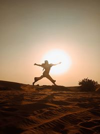 Silhouette man with arms outstretched against sky during sunset