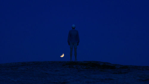 Rear view of man standing on land against sky at night