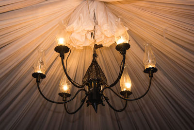 Low angle view of illuminated light bulb hanging on ceiling