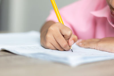 Cropped hand of girl writing on book at table