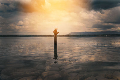 Man surfing in sea against sky during sunset